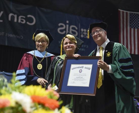 Professor of 职业治疗 Mary Siniscaro st和s between Provost Todd Pfannestiel 和 President Laura Casamento, 在2023年本科毕业典礼上颁奖.